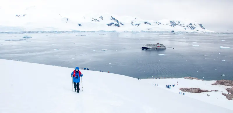Hikers climbing a snow slope in Antarctica, an expedition ship in the bay