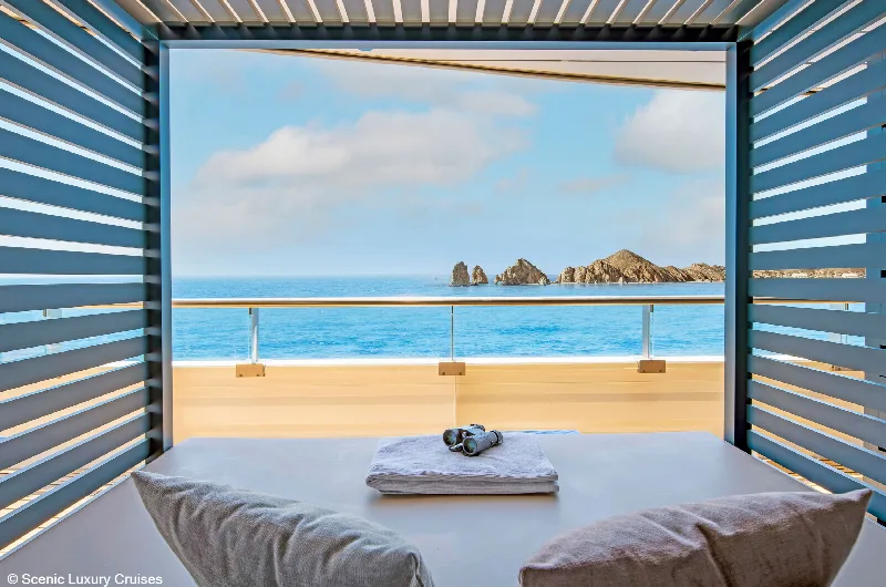 A private cabana on deck with a lounger, towel and sunglasses, the sea and a rocky coast behind