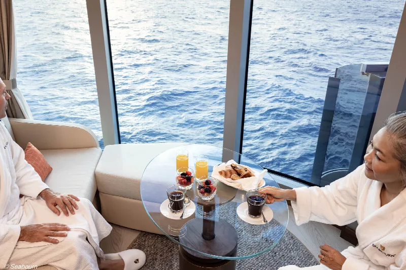 Two guests in bathrobes having breakfast at the panoramic window of a suite