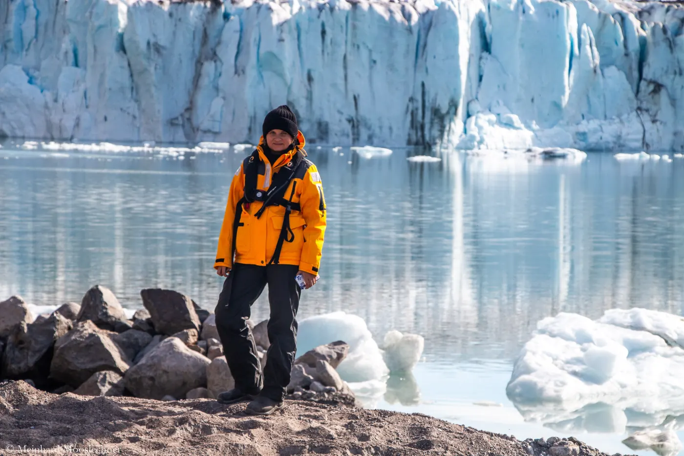 Daria Startseva in an orange expedition jacket in front of a glacier front in Greenland