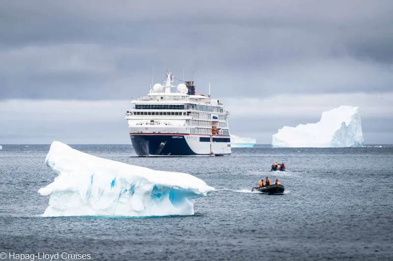 The expedition ship Hanseatic nature of Hapag-Lloyd Cruises among icebergs, with two Zodiacs in front