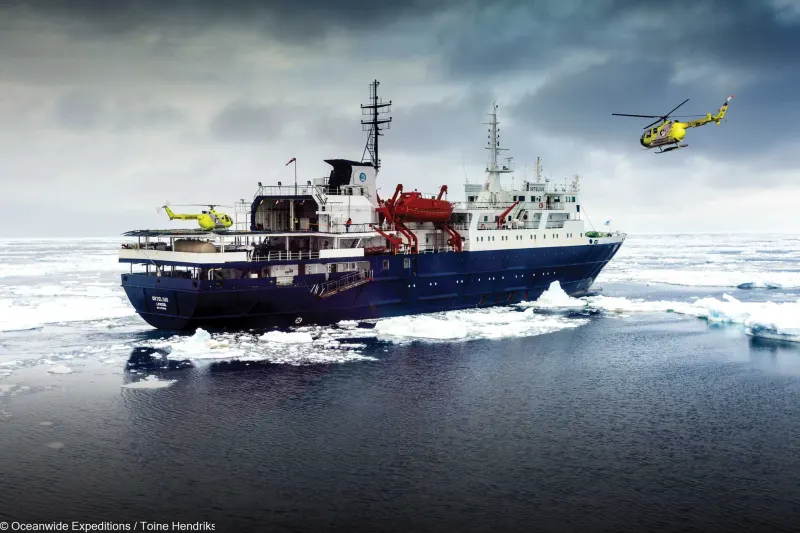 The expedition ship Ortelius of Oceanwide Expeditions in drift ice, one helicopter on deck and one in the air