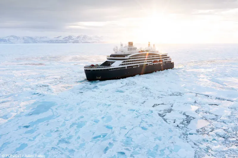 Le Commandant Charcot of PONANT in pack ice, with mountains and a low sun behind